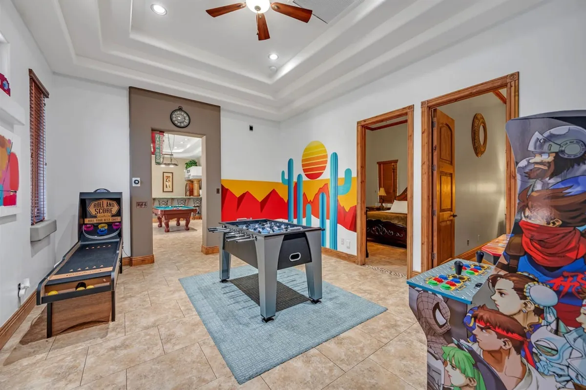 An interior view of the arcade/game room with a foosball table, arcade machine, and colorful wall mural. The space is lively and designed for both kids and adults to have fun and create lasting memories together.