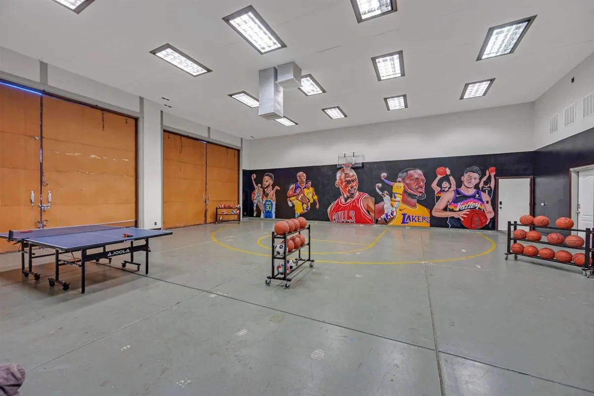 An energetic indoor recreation room featuring a basketball hoop with a mural of famous players, a ping pong table, and basketballs ready for action. The lively space is clearly designed for active group fun and friendly competition.