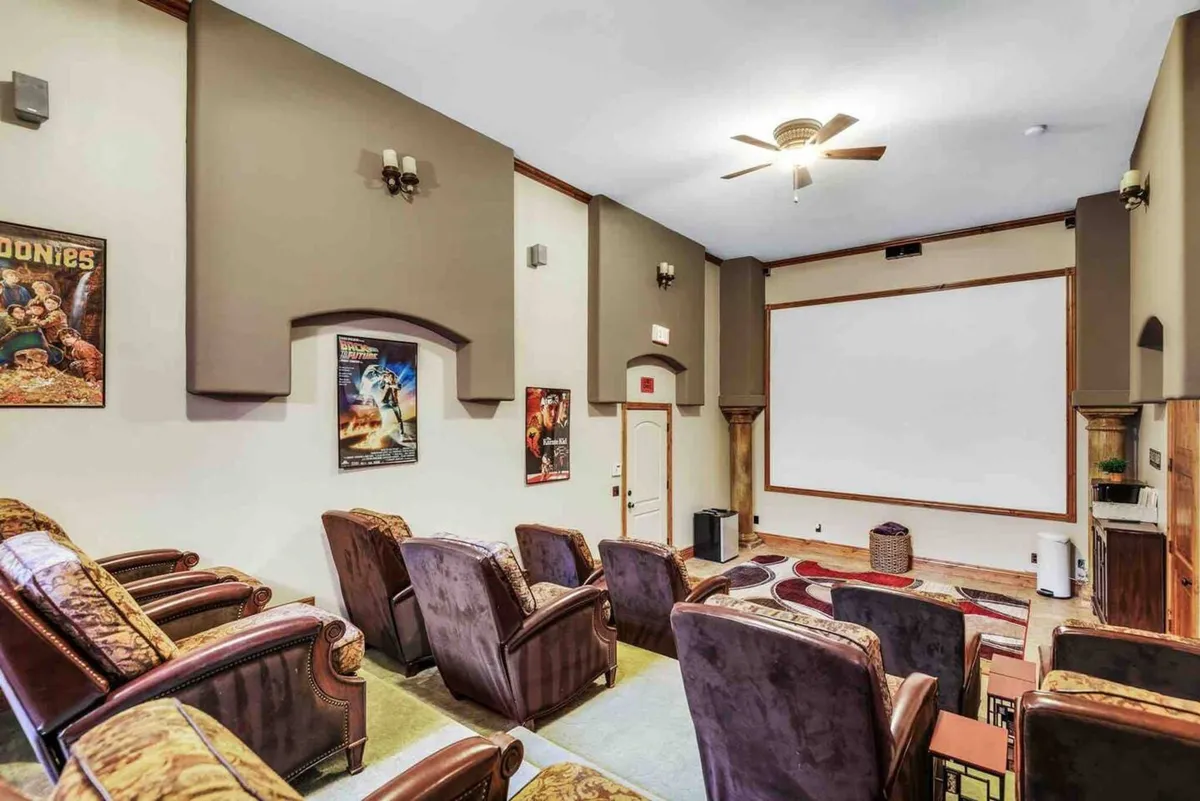 A dedicated home theater with rows of reclining chairs, a large projection screen, and classic movie posters on the walls. The space is designed for comfortable viewing and group enjoyment.