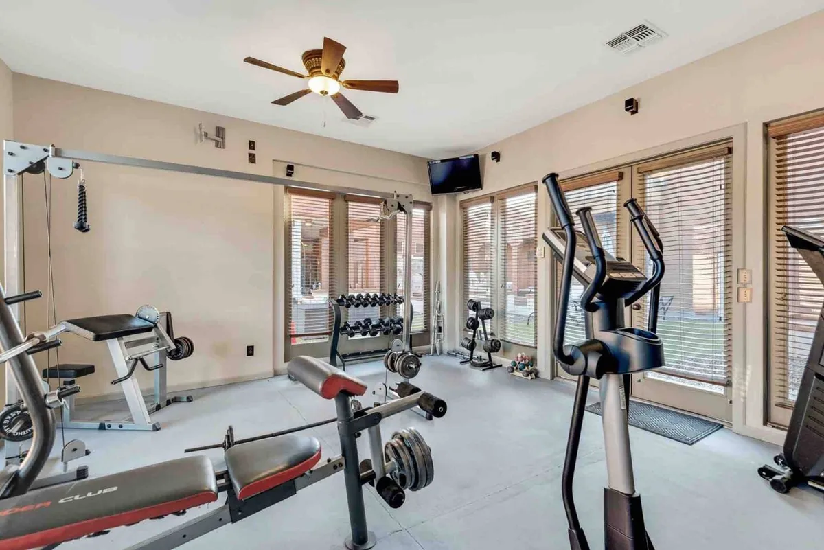 A view inside the private gym, with a weight bench, elliptical trainer, dumbbell rack, and large windows letting in ample natural light. The room is bright, modern, and designed for both cardio and strength workouts.