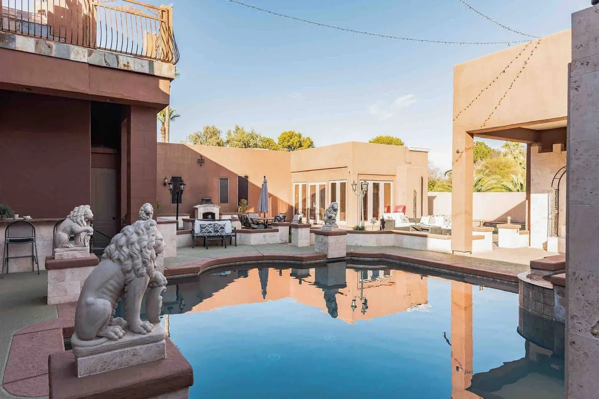 The photo features a luxurious outdoor swimming pool framed by lion statues, a fireplace, and an outdoor seating area. The setting is both elegant and relaxed, ideal for lounging, swimming, or hosting an evening barbecue under the stars.