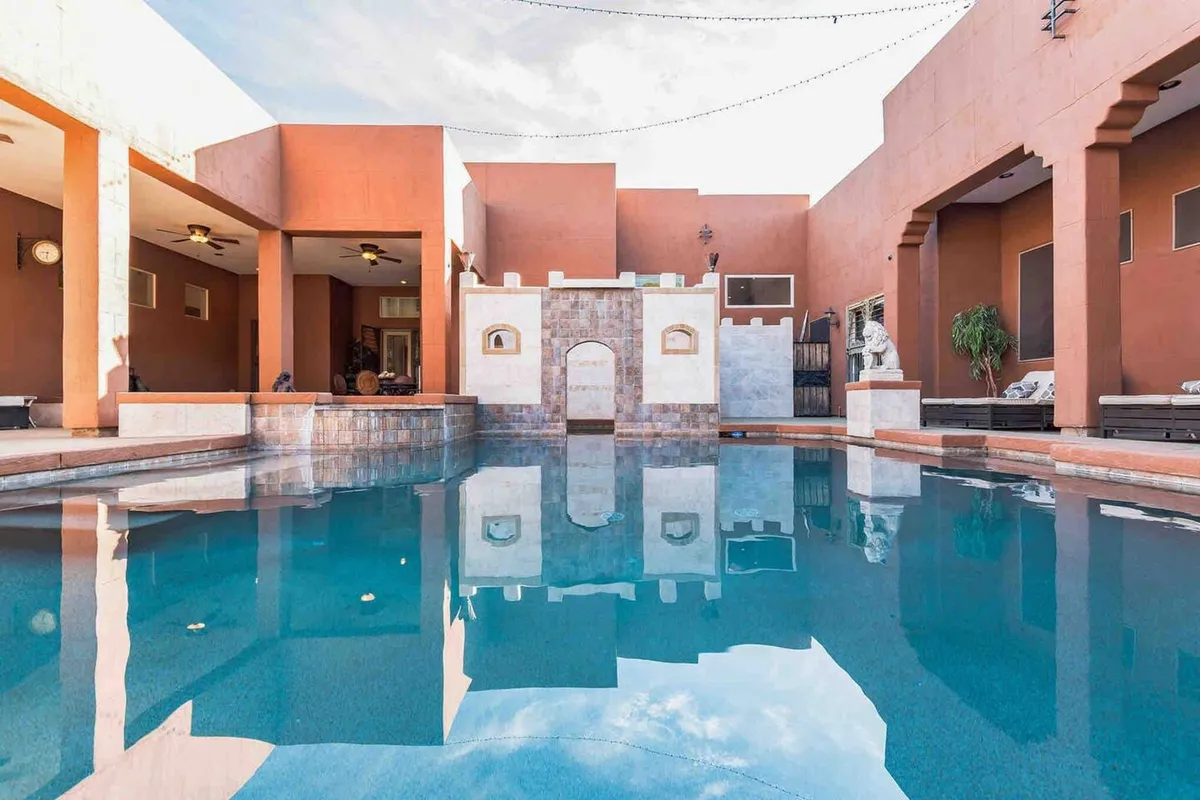 A tranquil exterior view featuring a sparkling swimming pool as the focal point. The scene includes a decorative wall, an inviting outdoor seating area with lounge chairs, and lush surroundings—all bathed in natural light, suggesting a relaxing, resort-like atmosphere.