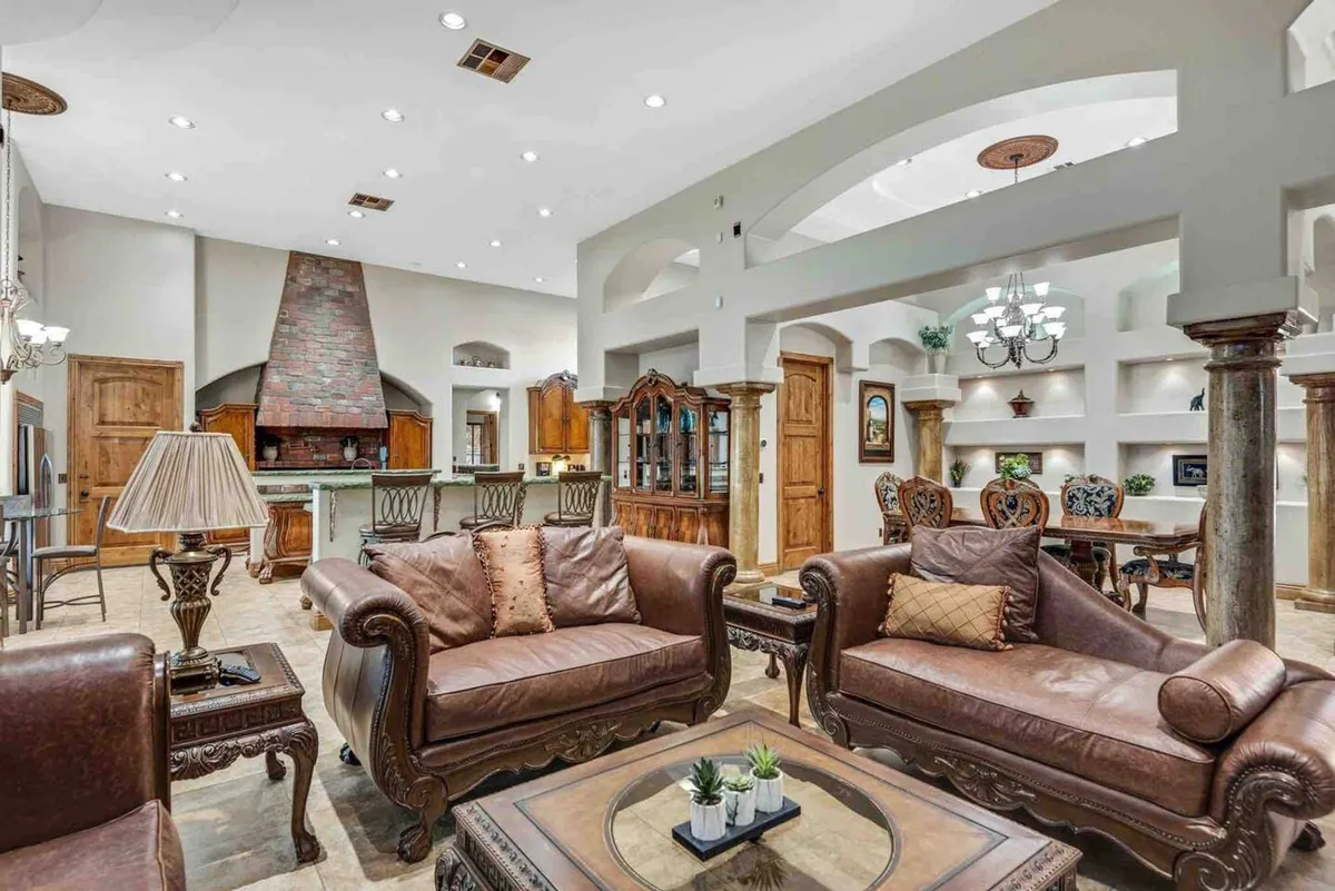 This image showcases a luxurious living room with leather sofas, a central coffee table, an ornate chandelier, and arched ceilings. The setup suggests a welcoming atmosphere ideal for large gatherings and socializing.