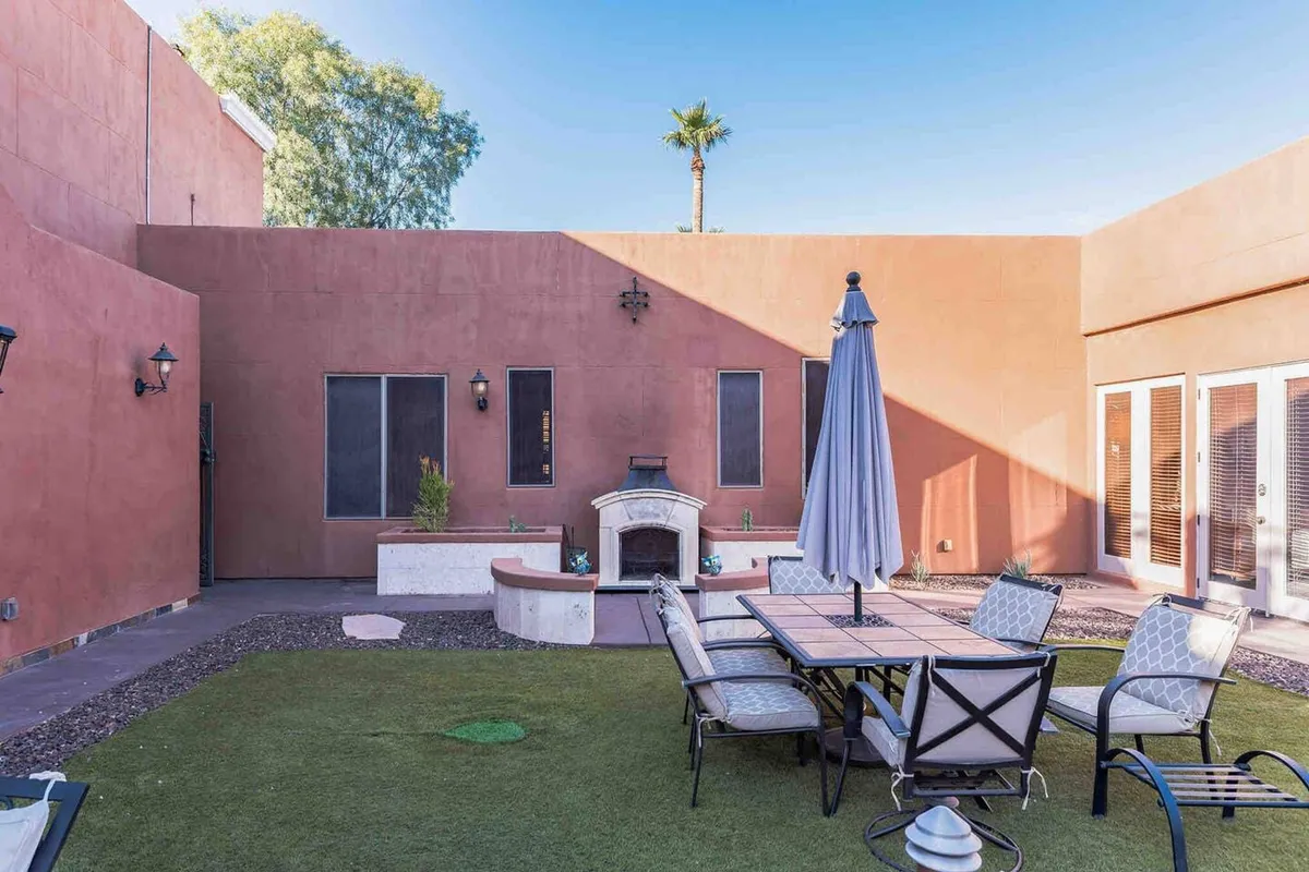 A spacious outdoor dining setup with a fireplace and umbrella, surrounded by palm trees. The setting suggests comfortable alfresco dining and relaxed gatherings, ideal for enjoying meals prepared in the gourmet kitchen.